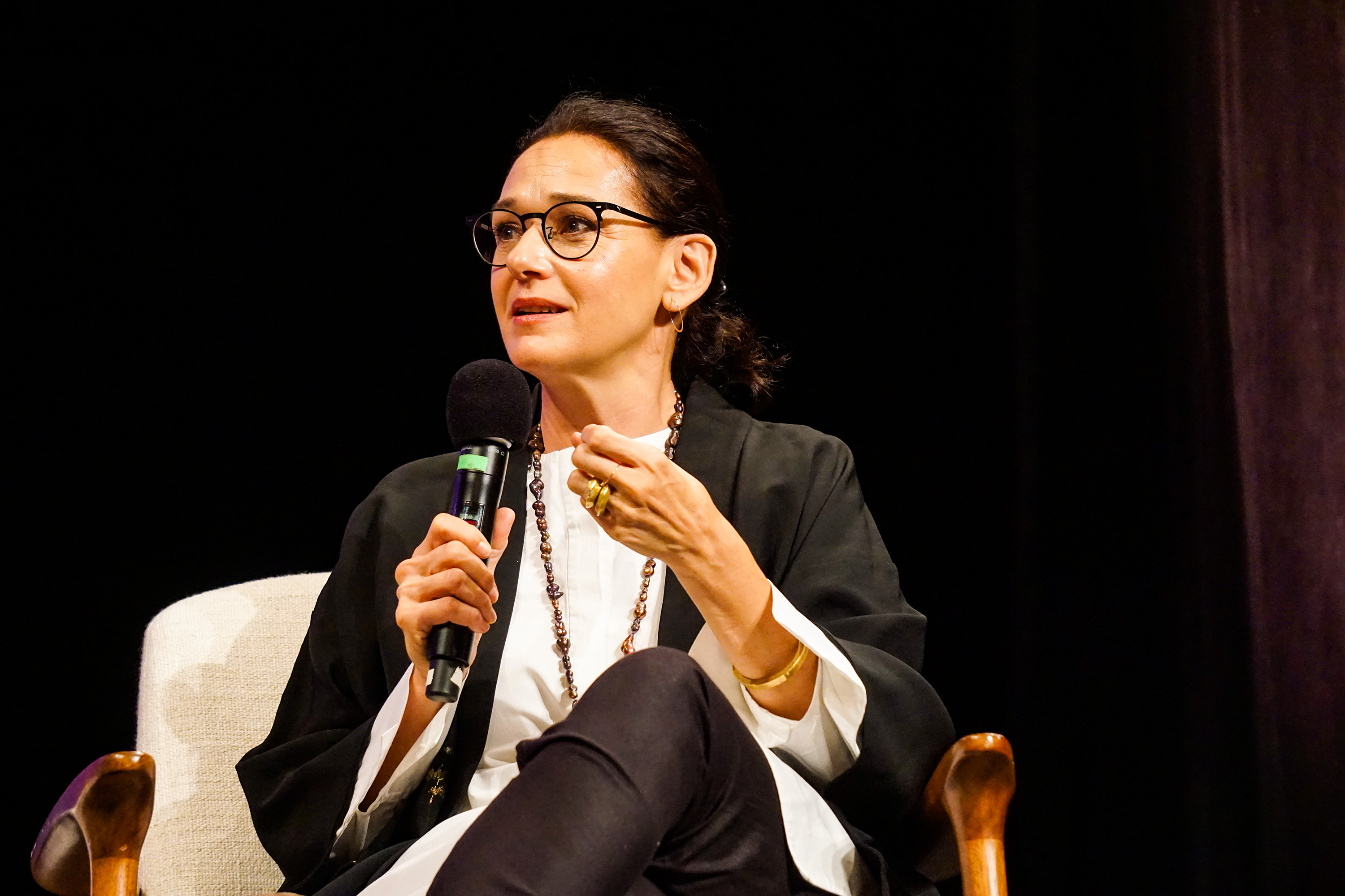 Carmen Artigas sitting with the microphone on stage making a point by gesticulating with her hand