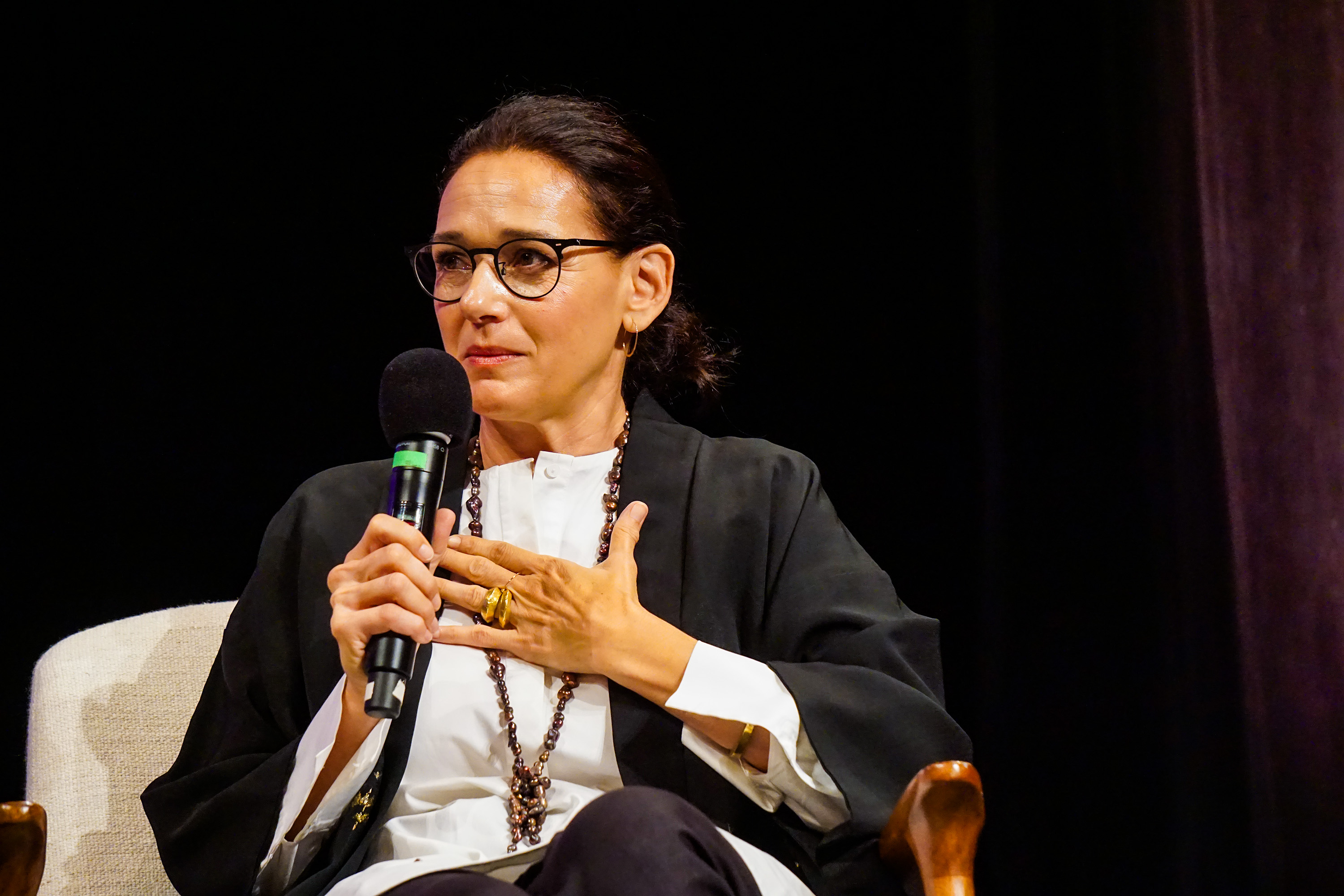 Carmen Artigas sitting with the microphone on stage gesturing with her hand