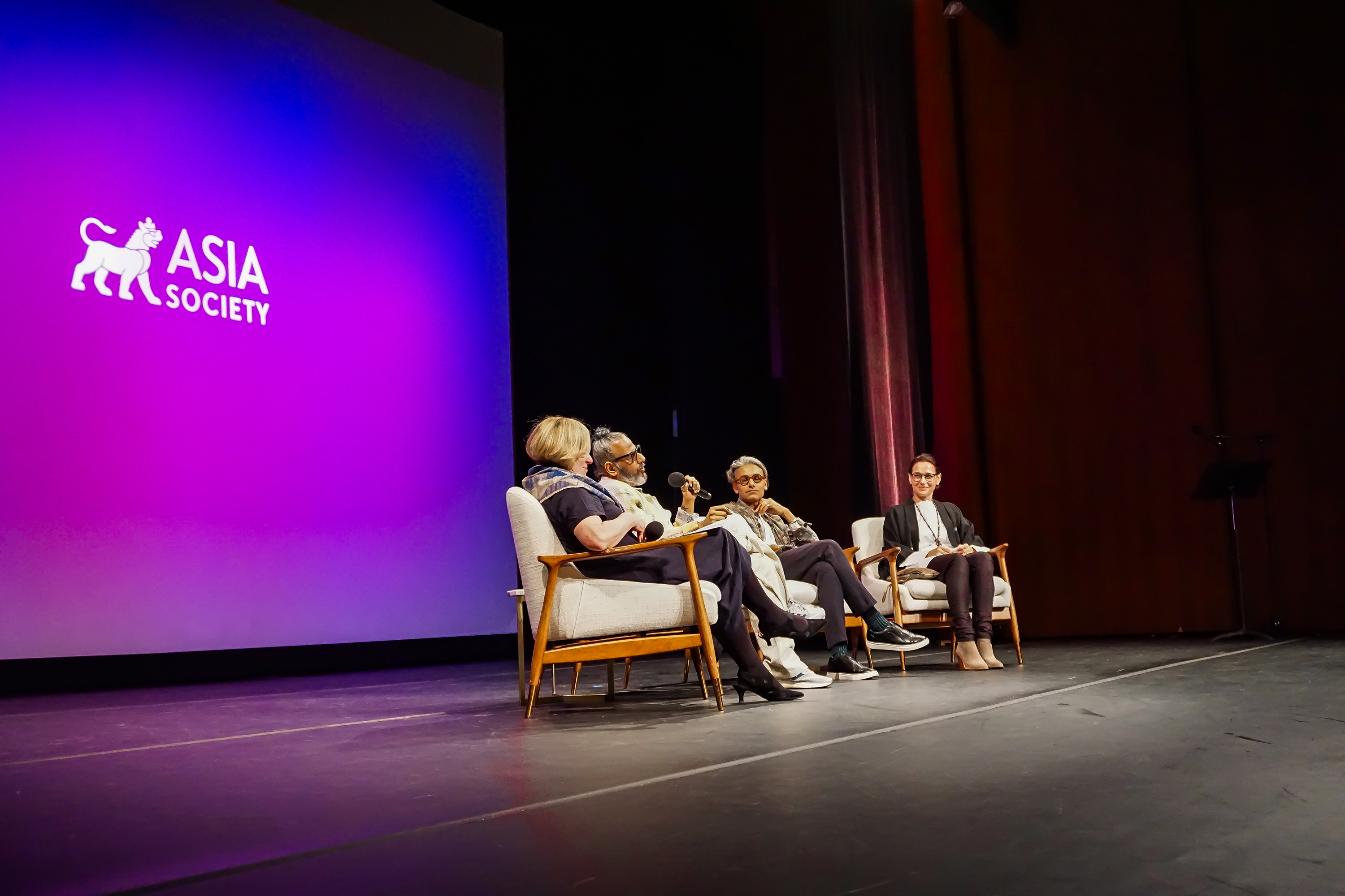 Distant Ajay Shrivastav, Carmen Artigas Sandy Dalal, Rachel Cooper sitting on stage with a purple background with Asia Society logo