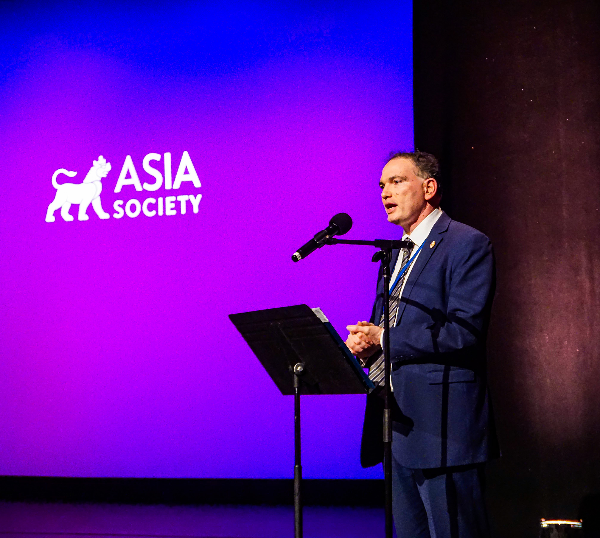 A representative from the NYC government speaking at the podium with a purple background and Asia Society logo