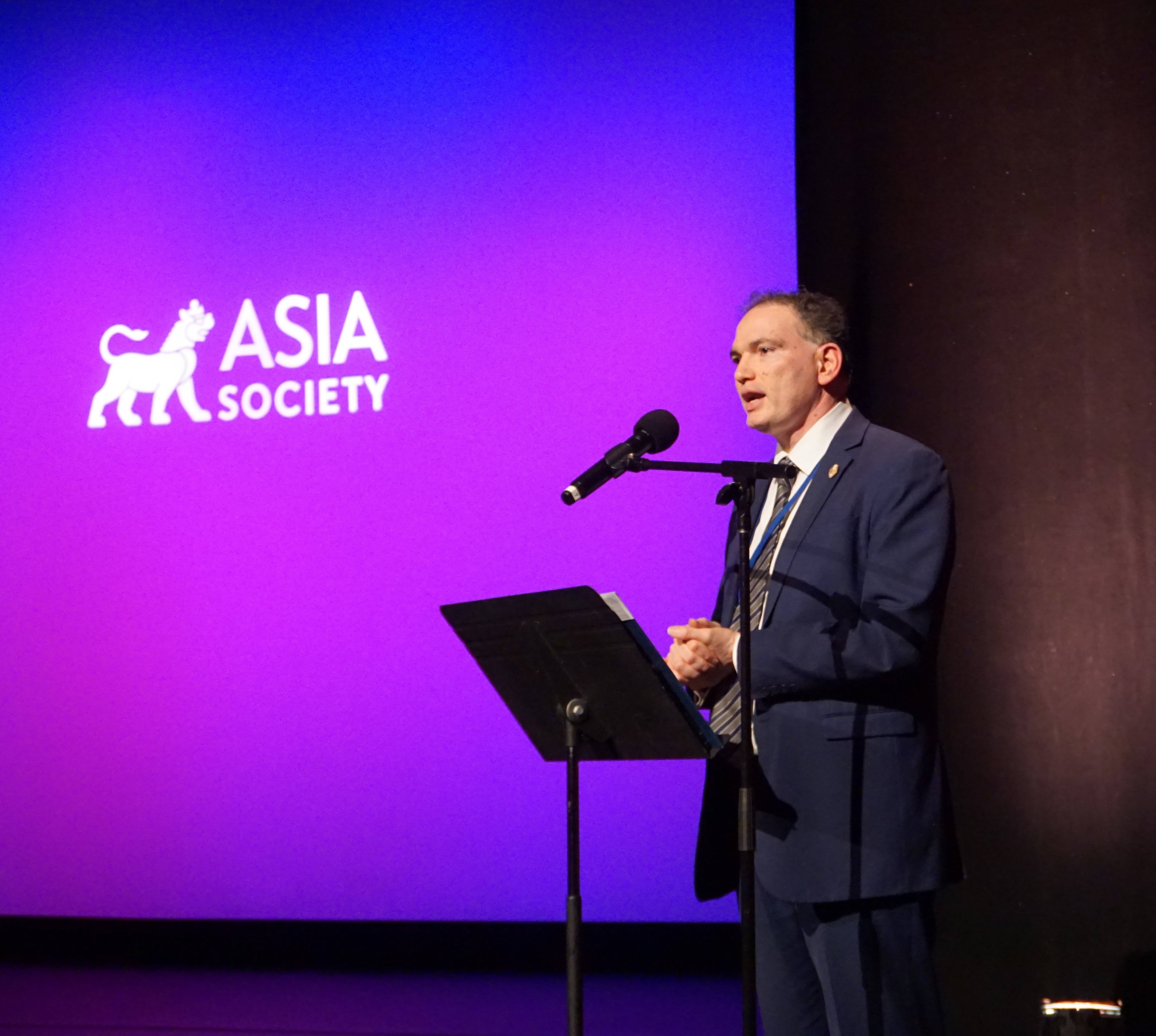 New York government representative speaking at podium on stage with Asia Society logo in purple background