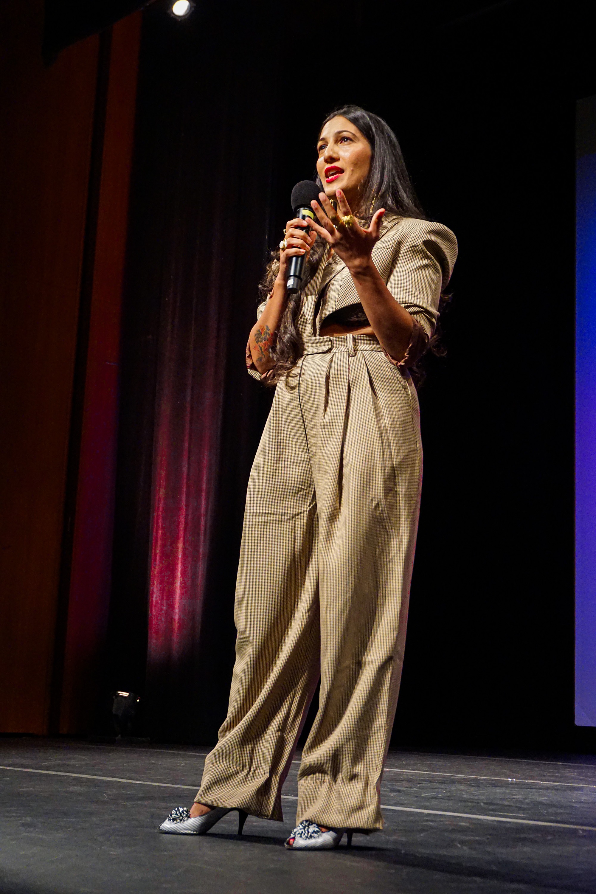 Full body of Poonam Thimmaiah on stage speaking into the microphone with her hand out