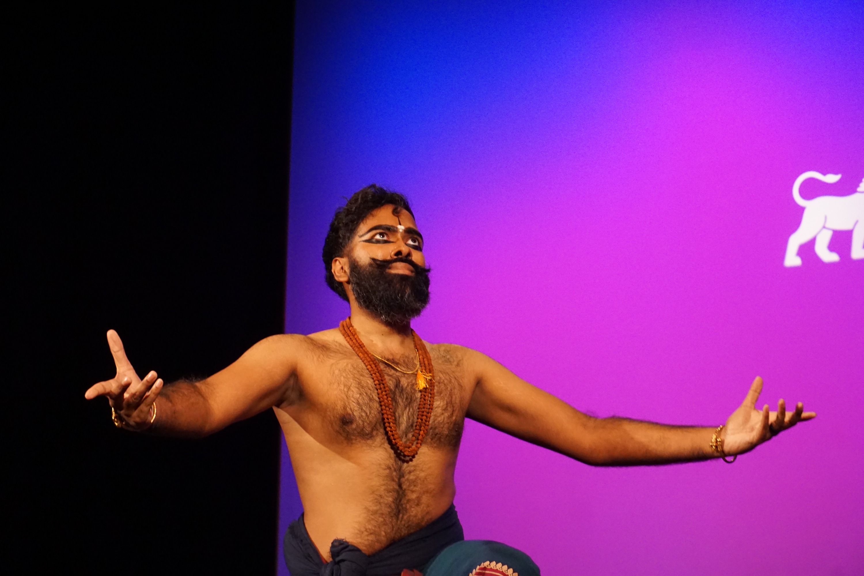 Jeeno Joseph on his knees with his arms spread wide apart on stage against a purple background