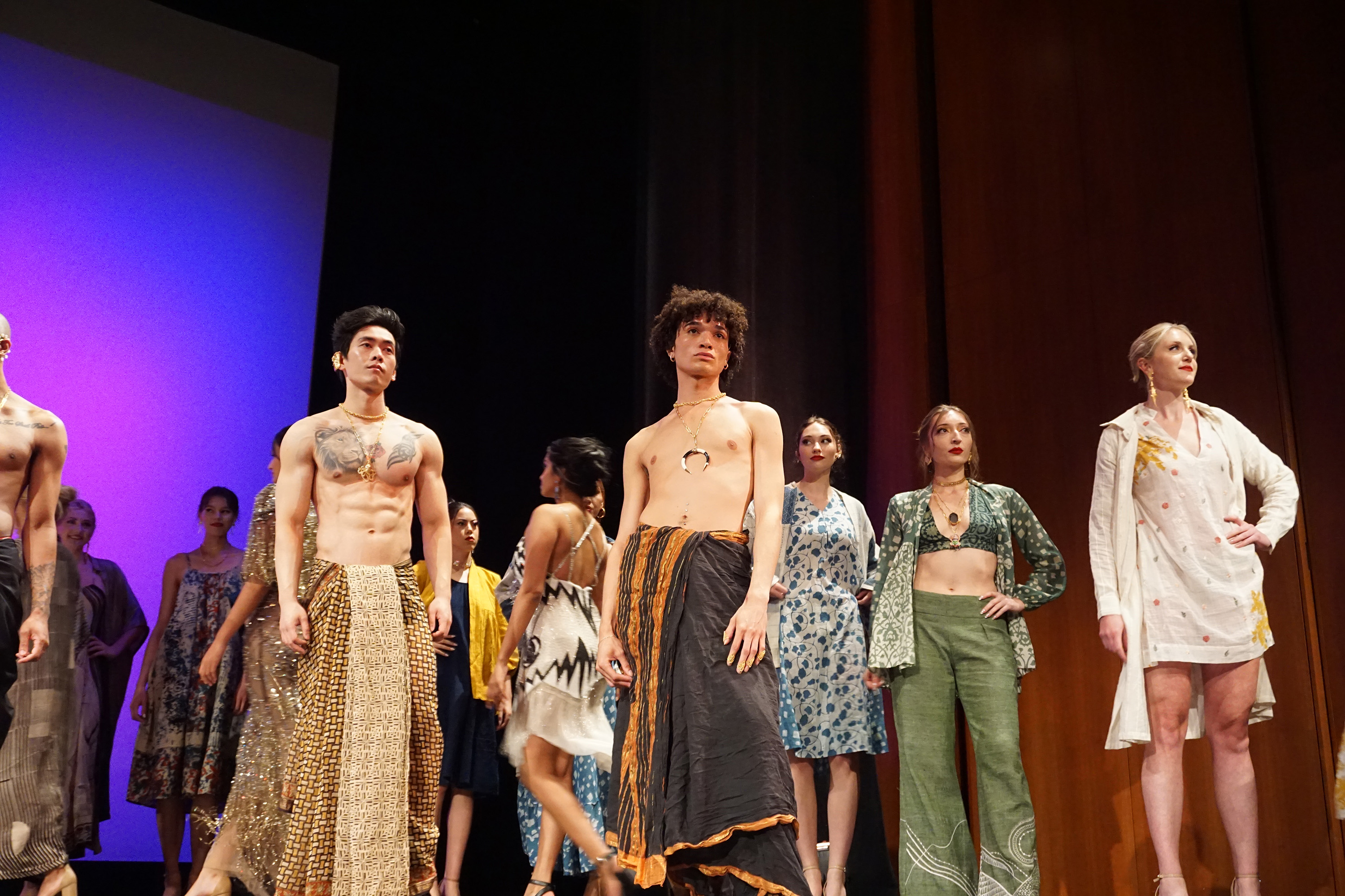 Crowd of models standing on stage with two shirtless male male models standing prominently in front