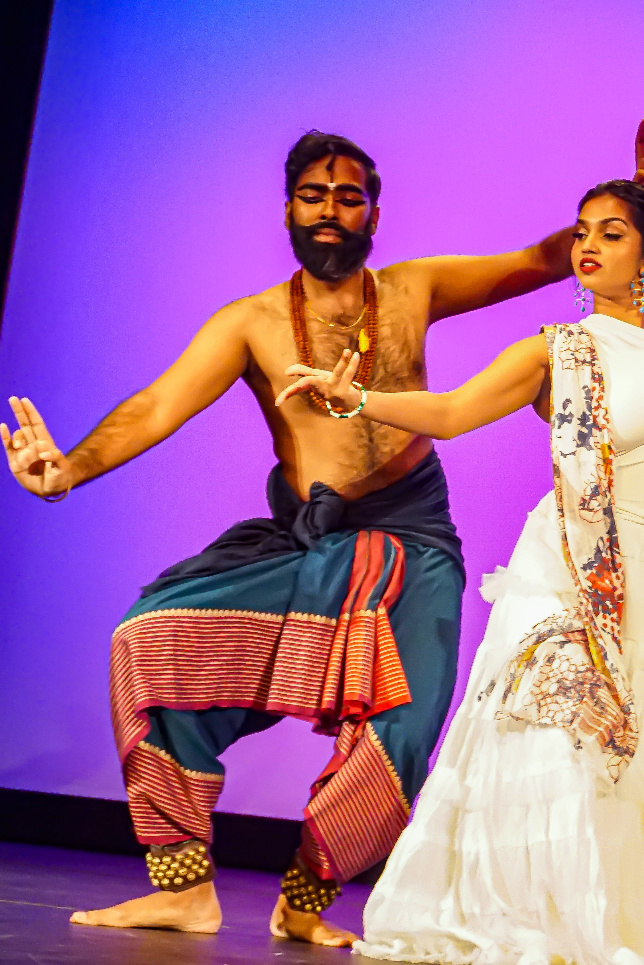 Jeeno Joseph dancing with his female counterpart with both of their arms stretched out on stage against purple background