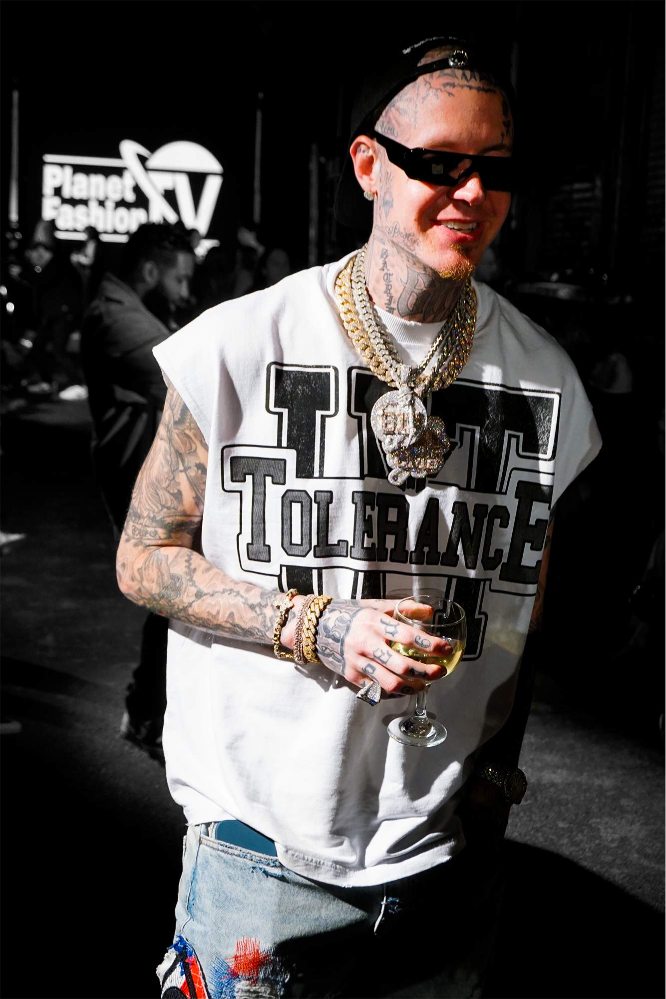 Millyz standing holding a cup outdoors in night time smiling wearing his chain