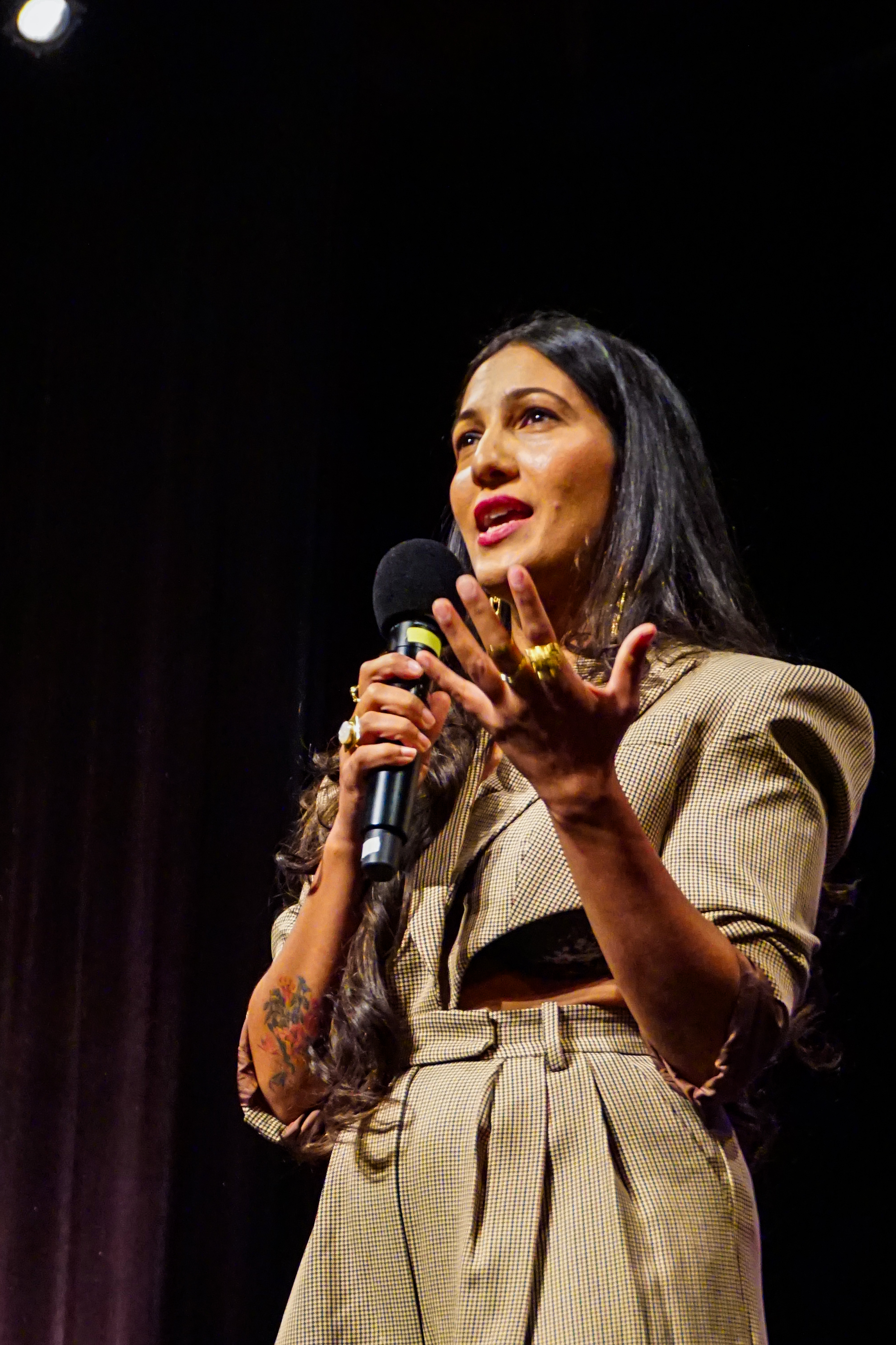 Close up of Poonam Thimmaiah on stage speaking into the microphone with her hand out