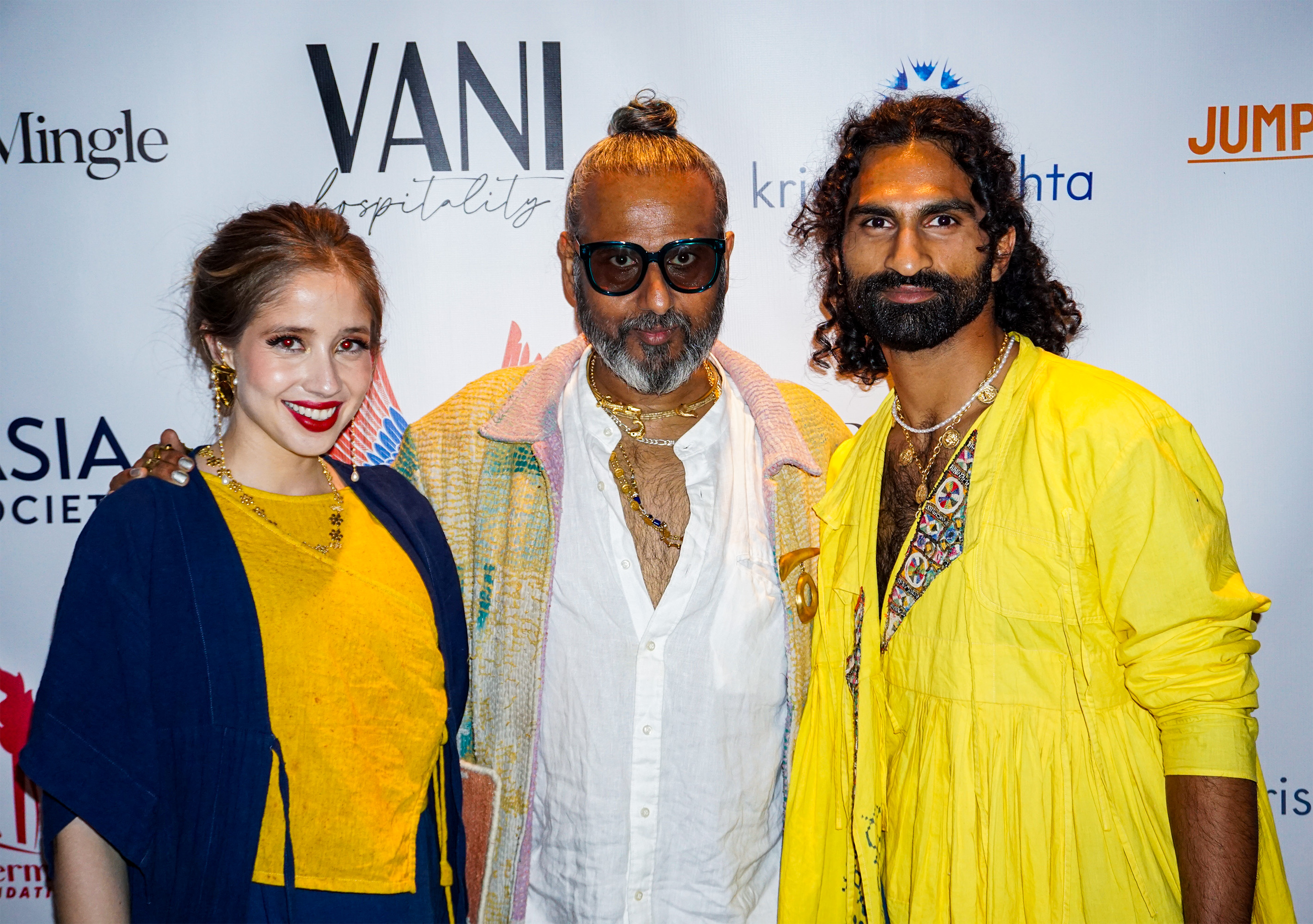 Ajay Shrivastav in between a male and female model wearing yellow clothing in front of a step and repeat banner