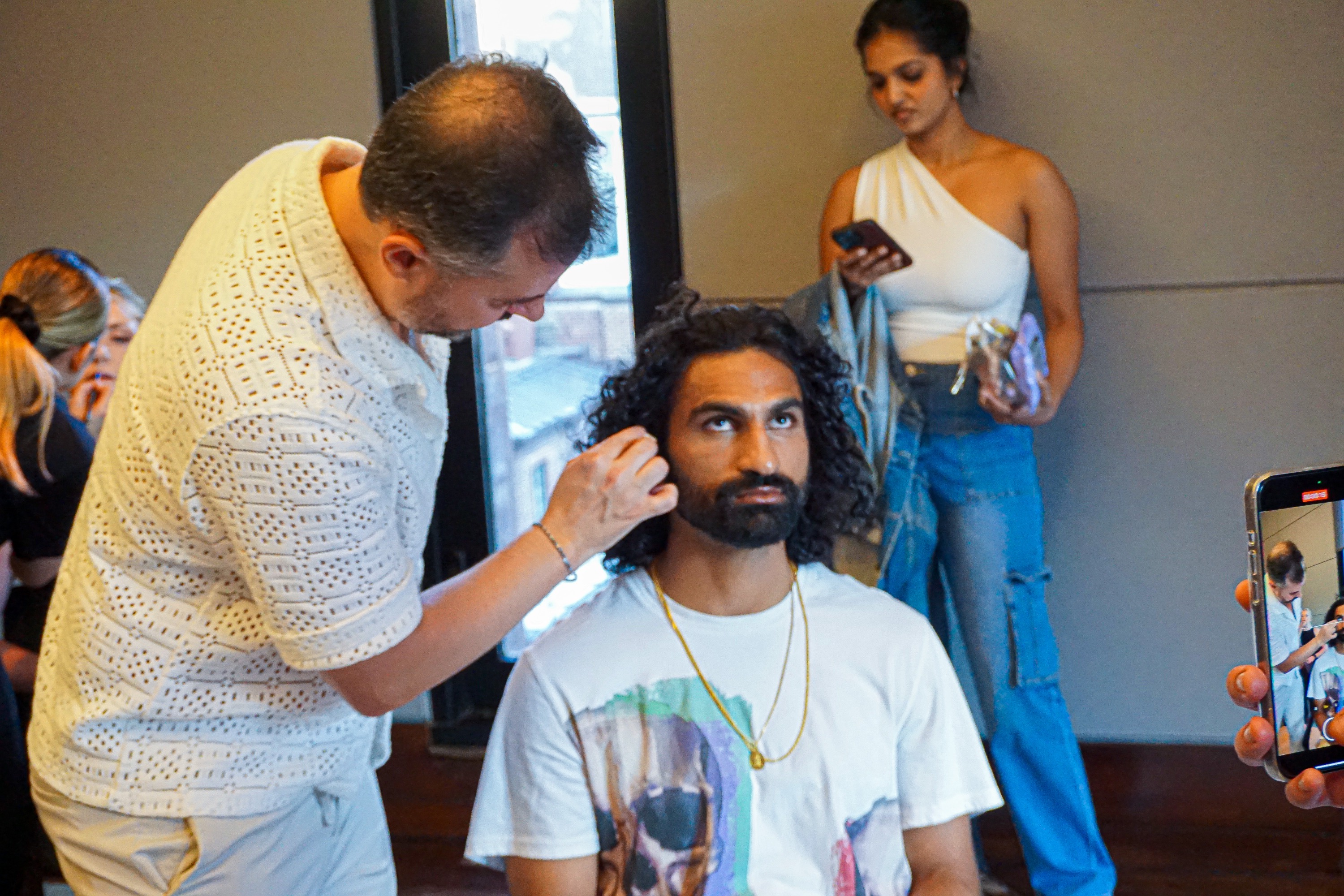 a male model getting his make up done by a male make up artist and a female model standing in the background