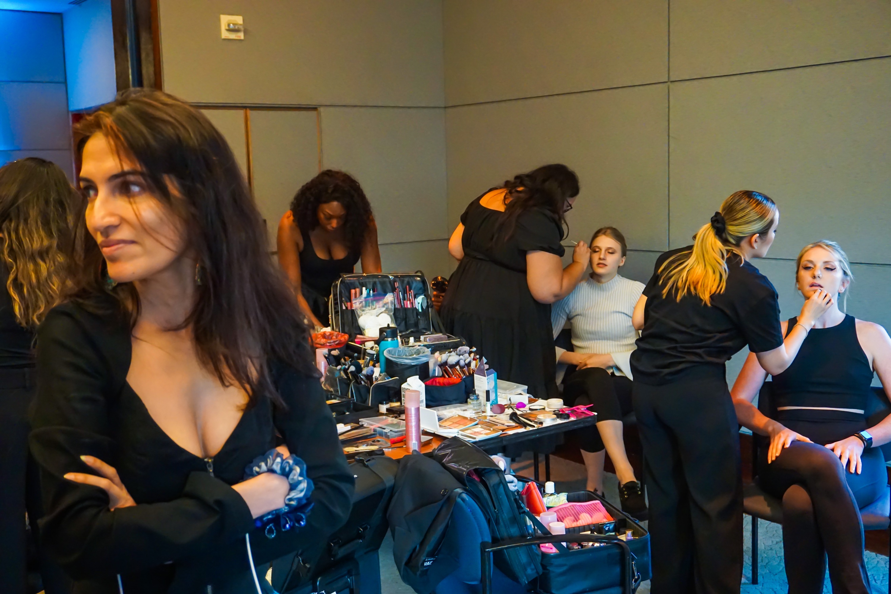 A backstage scene of hair and make up models busy at work with models and a woman looking off to the side