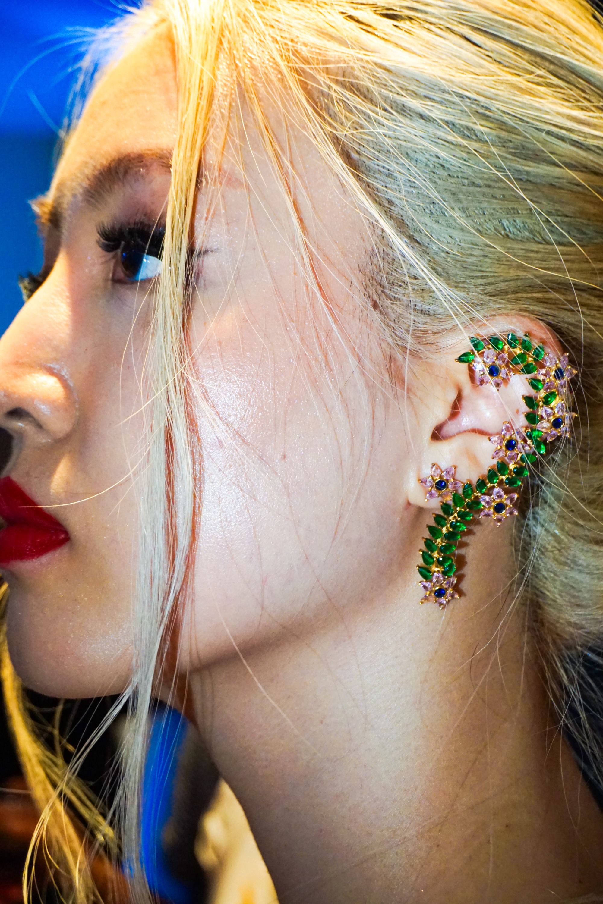 Sideview close up a female model and blonde hair wearing large decorative green earrings