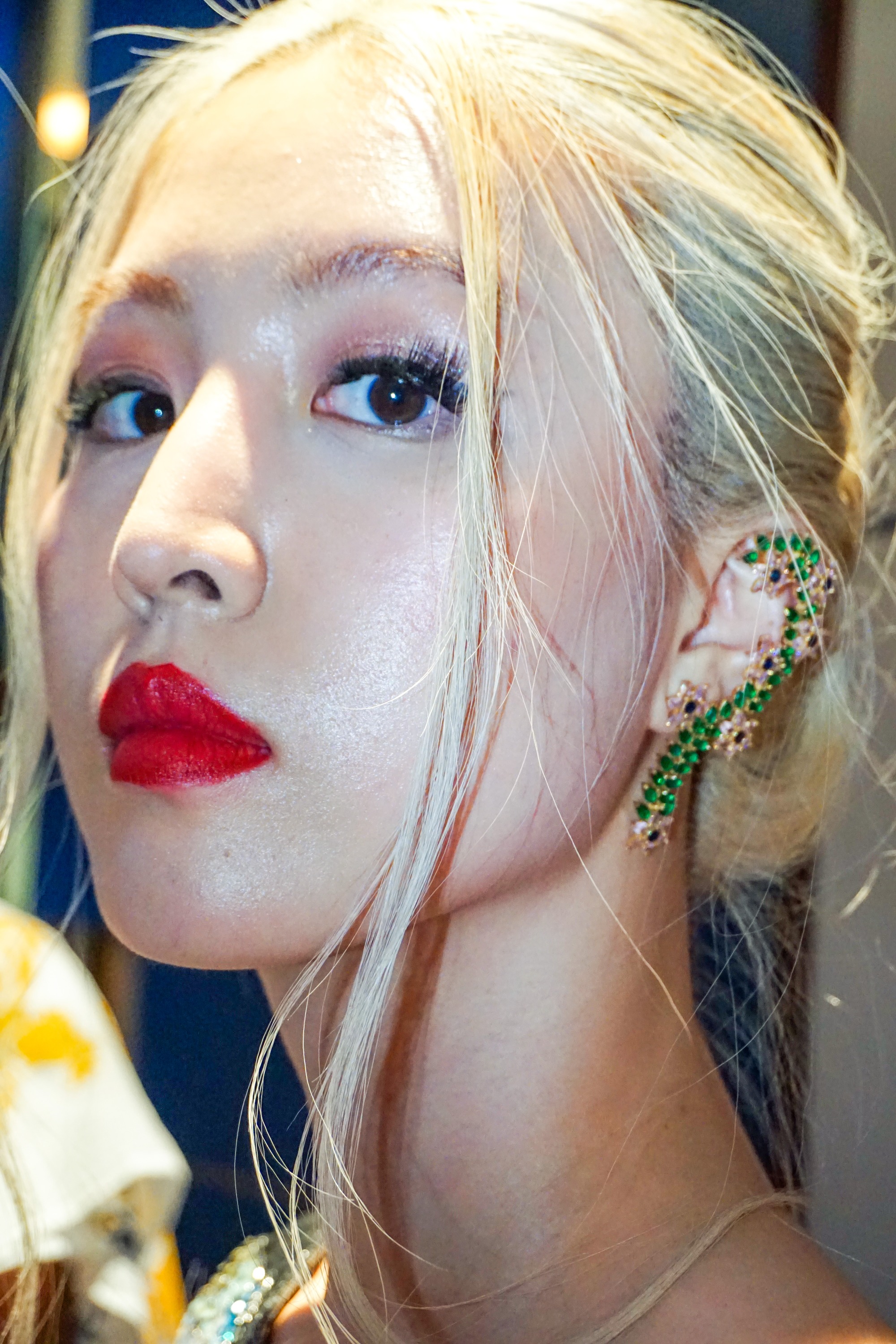 Close up an Asian woman with red lipstick and blonde hair wearing large decorative green earrings made by Maalicious jewelry