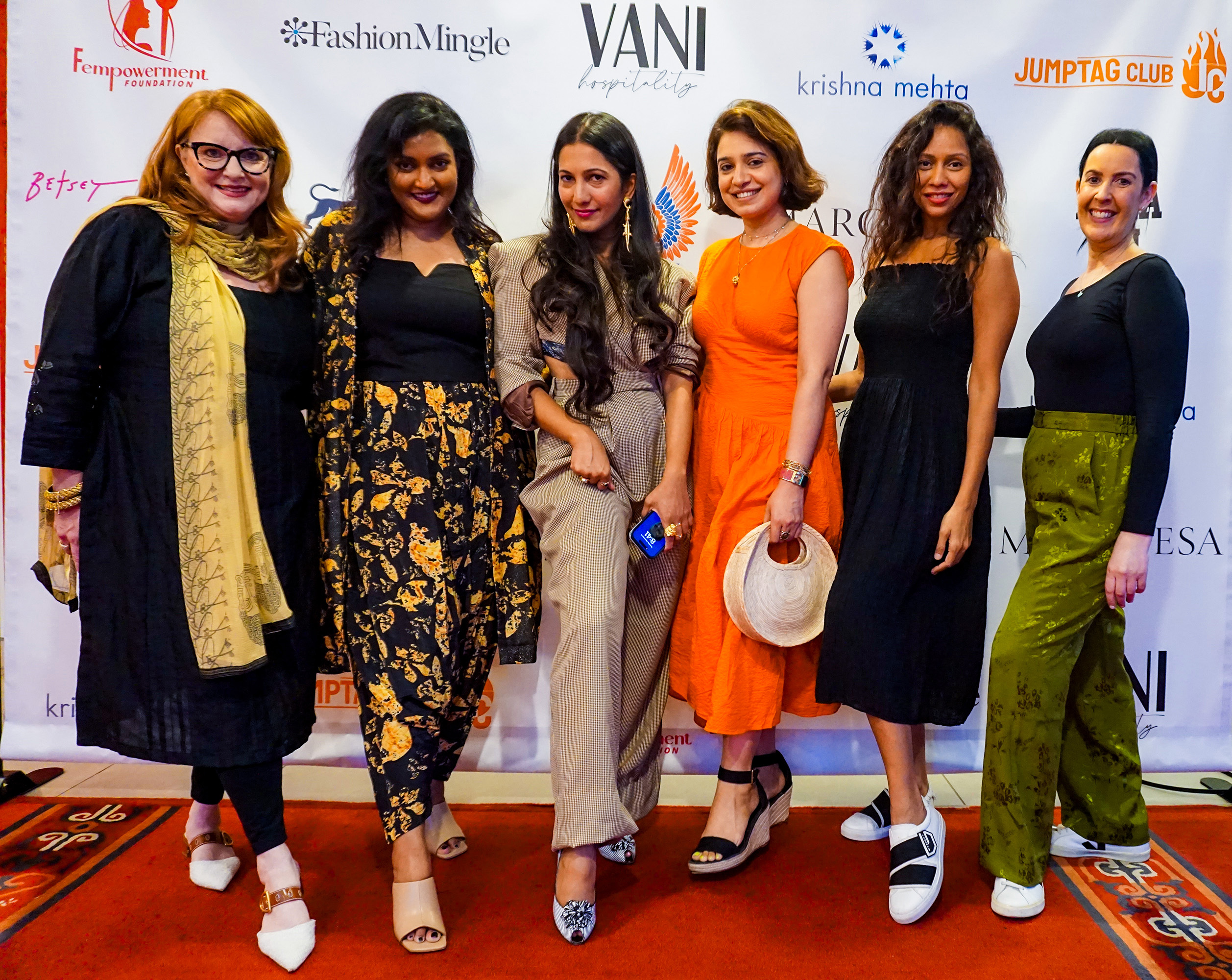 Melissa Shea, Poonam Thimmaiah, Sneha Andani and others posing together with their shoes prominently in view in front of a step and repeat banner