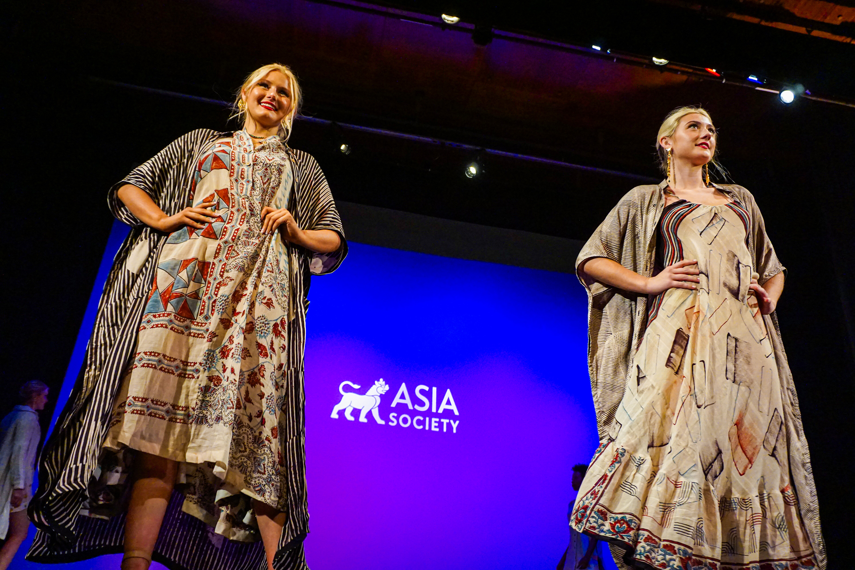 Two female fashion models on stage posing for the audience with hands on hips in Indian style dresses