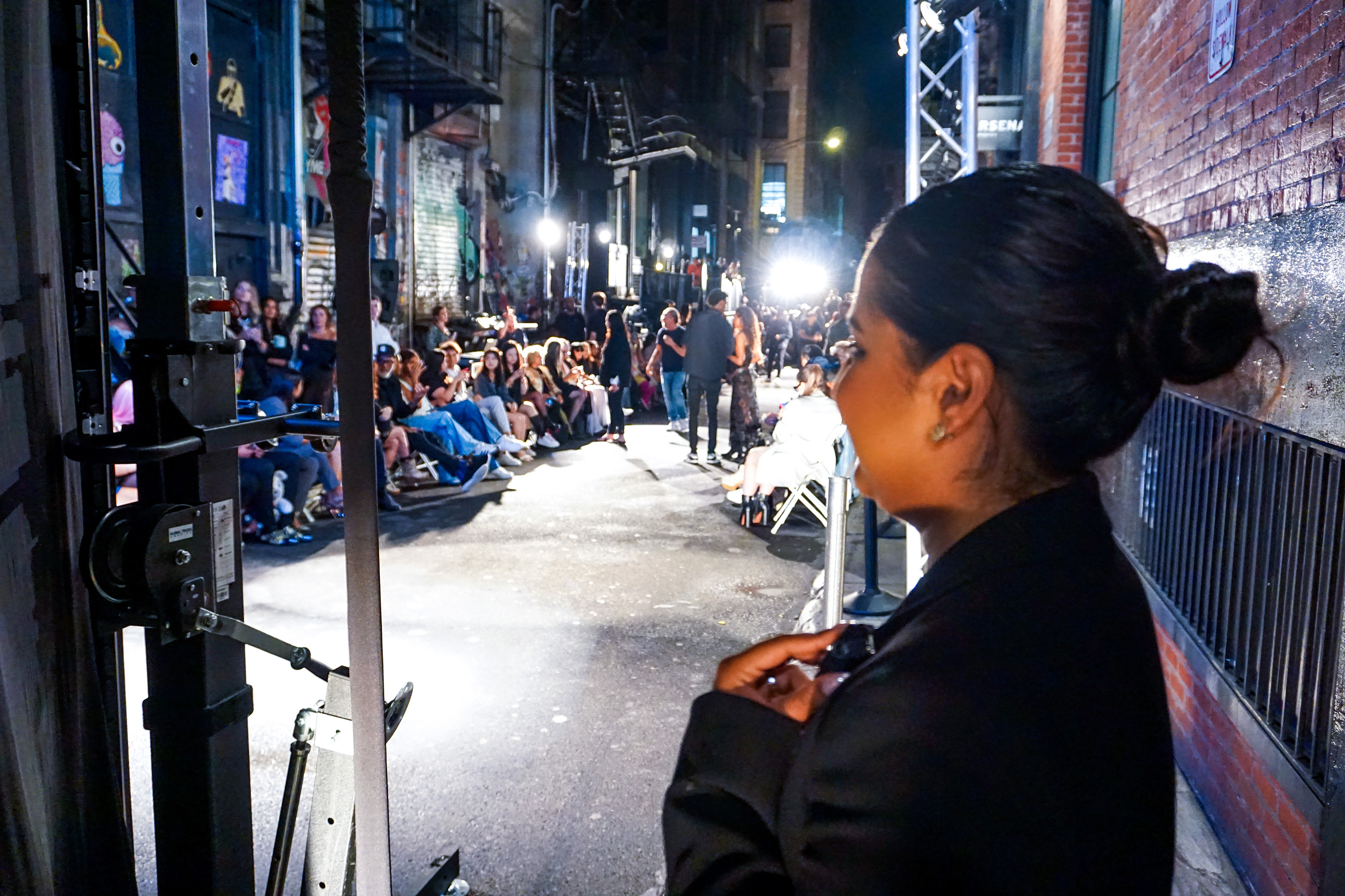 An outdoor night time fashion show with a female security guard front of backstage entrance at Walker Hotel New York