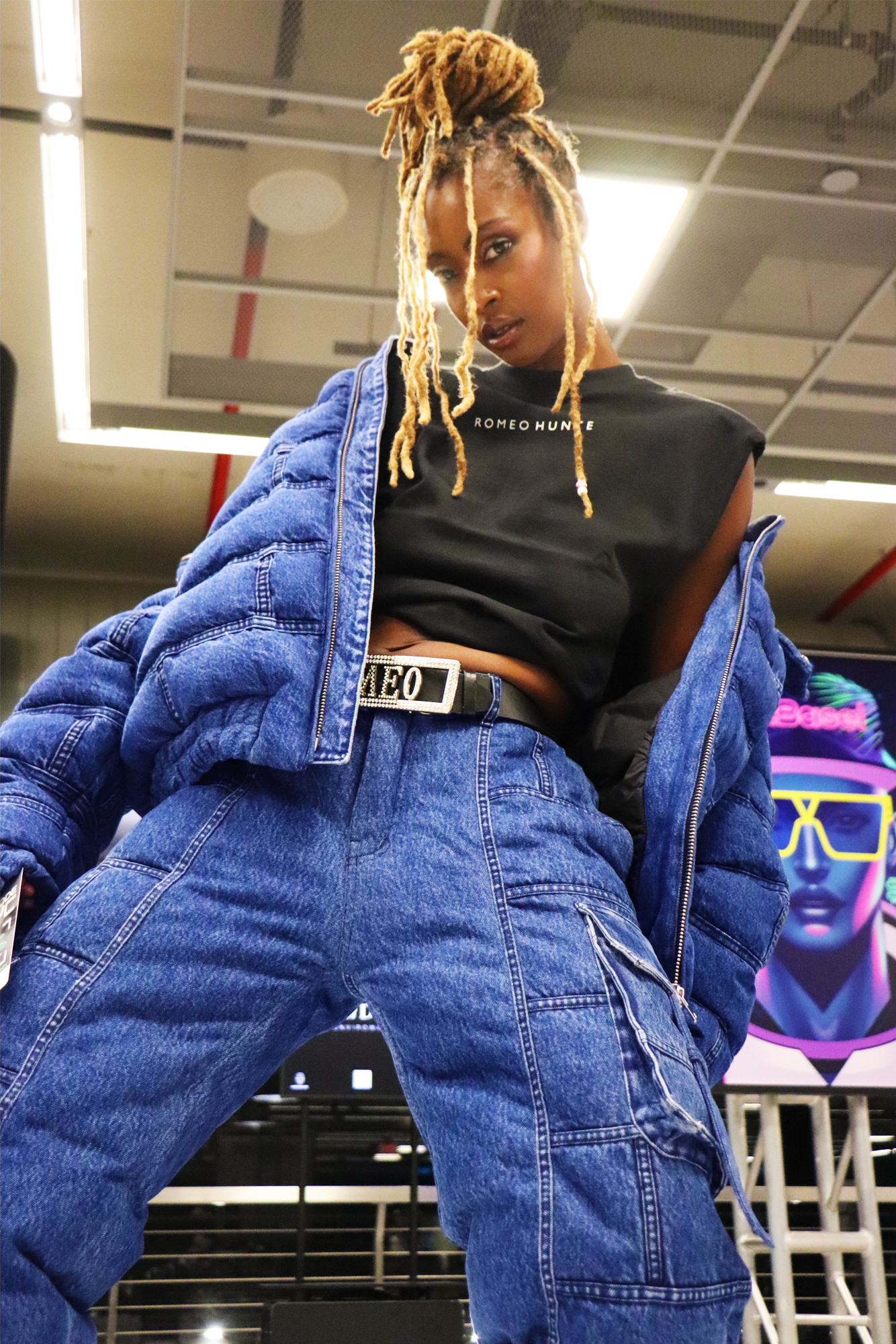 African American female model wearing denim Romeo Hunte pants and jacket leaning back posing for the camera with wide stance