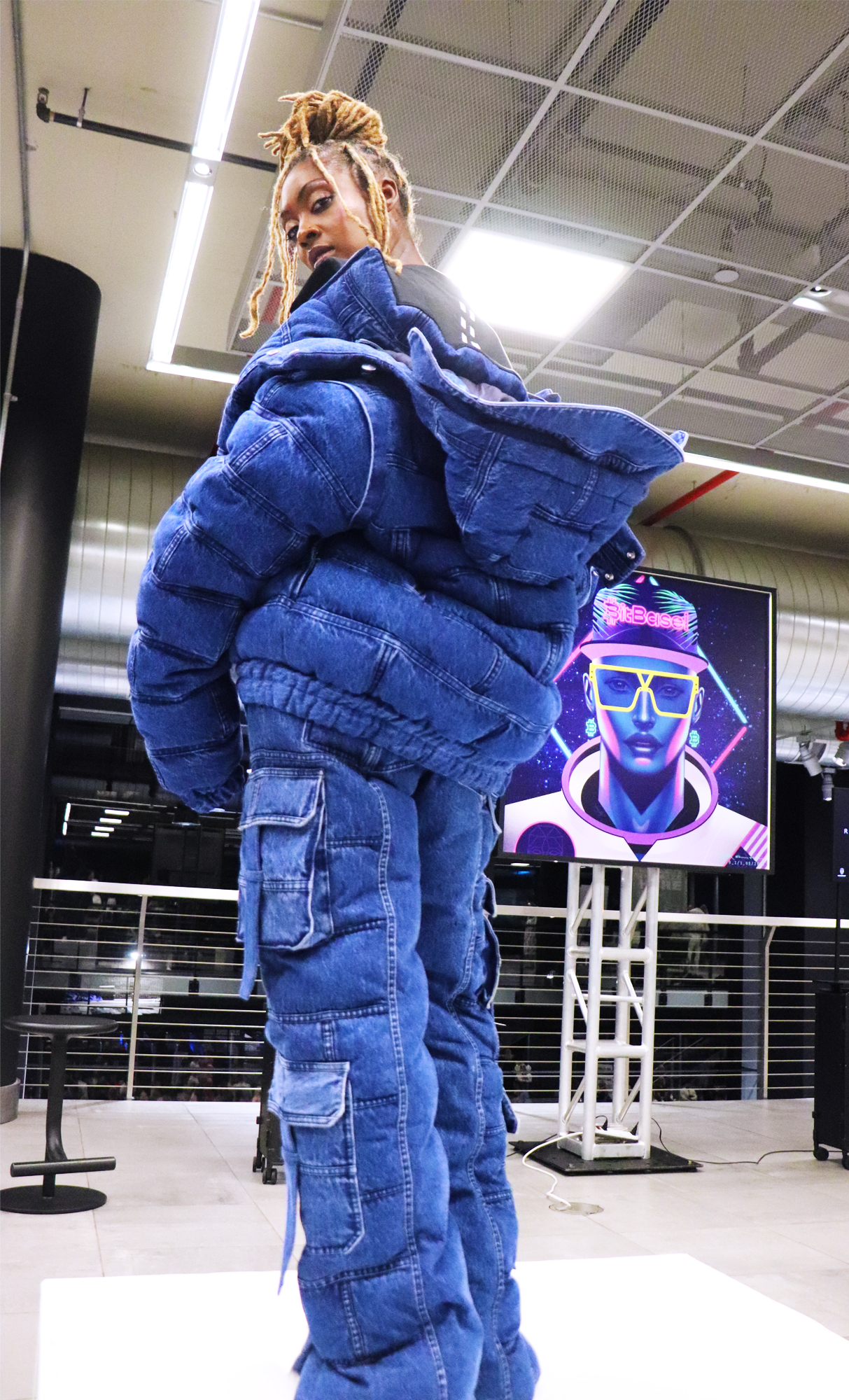 Am african american female model wearing a blue denim jacket and pants by Romeo Hunte looking back turned to the camera