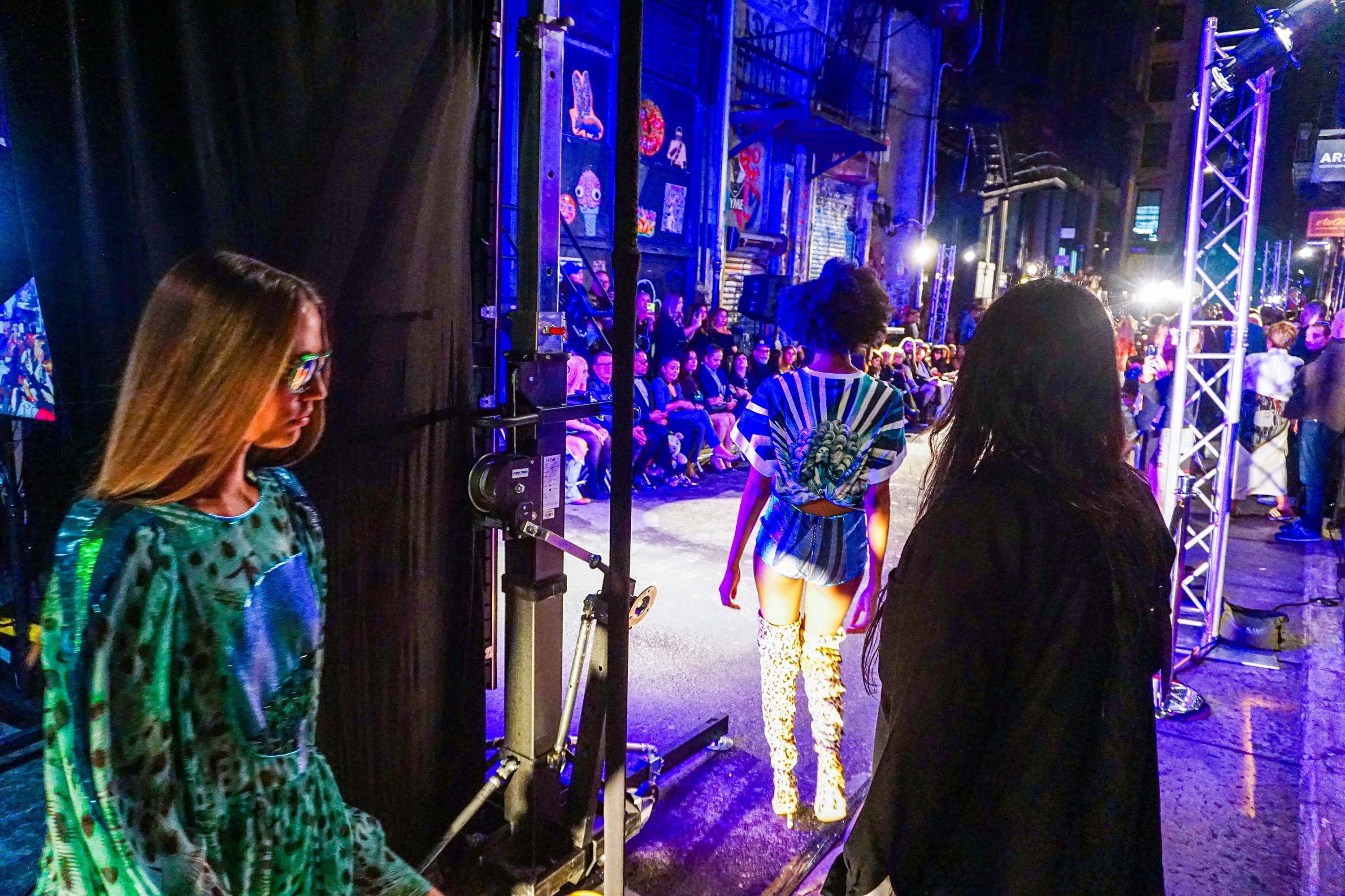 Models walking backstage toward the blue lit runway outside