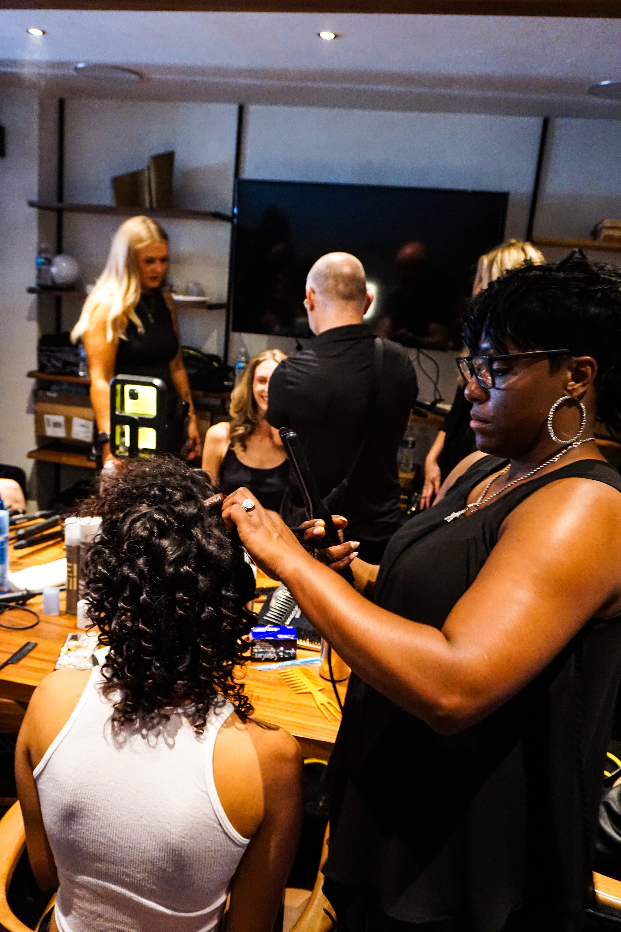 African-American hair stylist working with a model's hair in a busy room