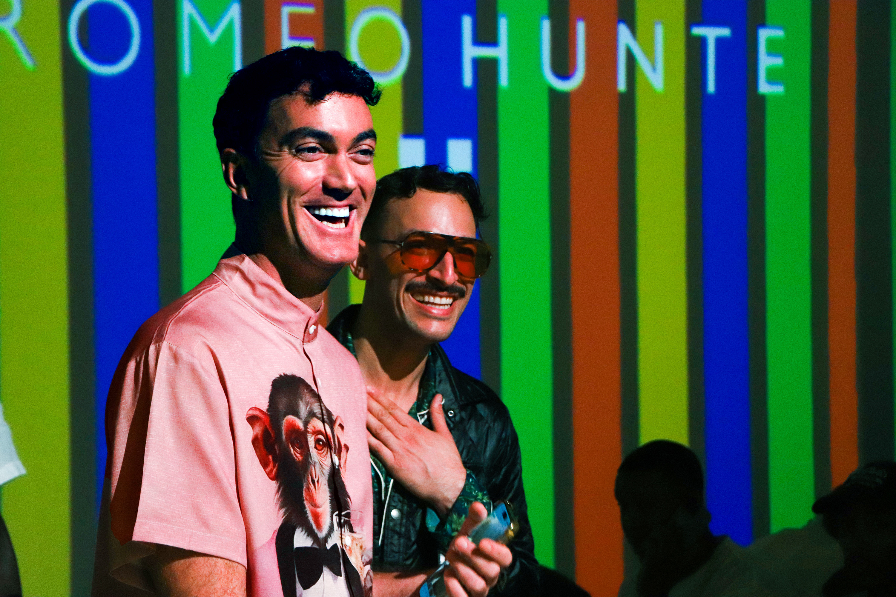 Matt Dillon and friend standing at Romeo Hunte's fashion show in front of his logo