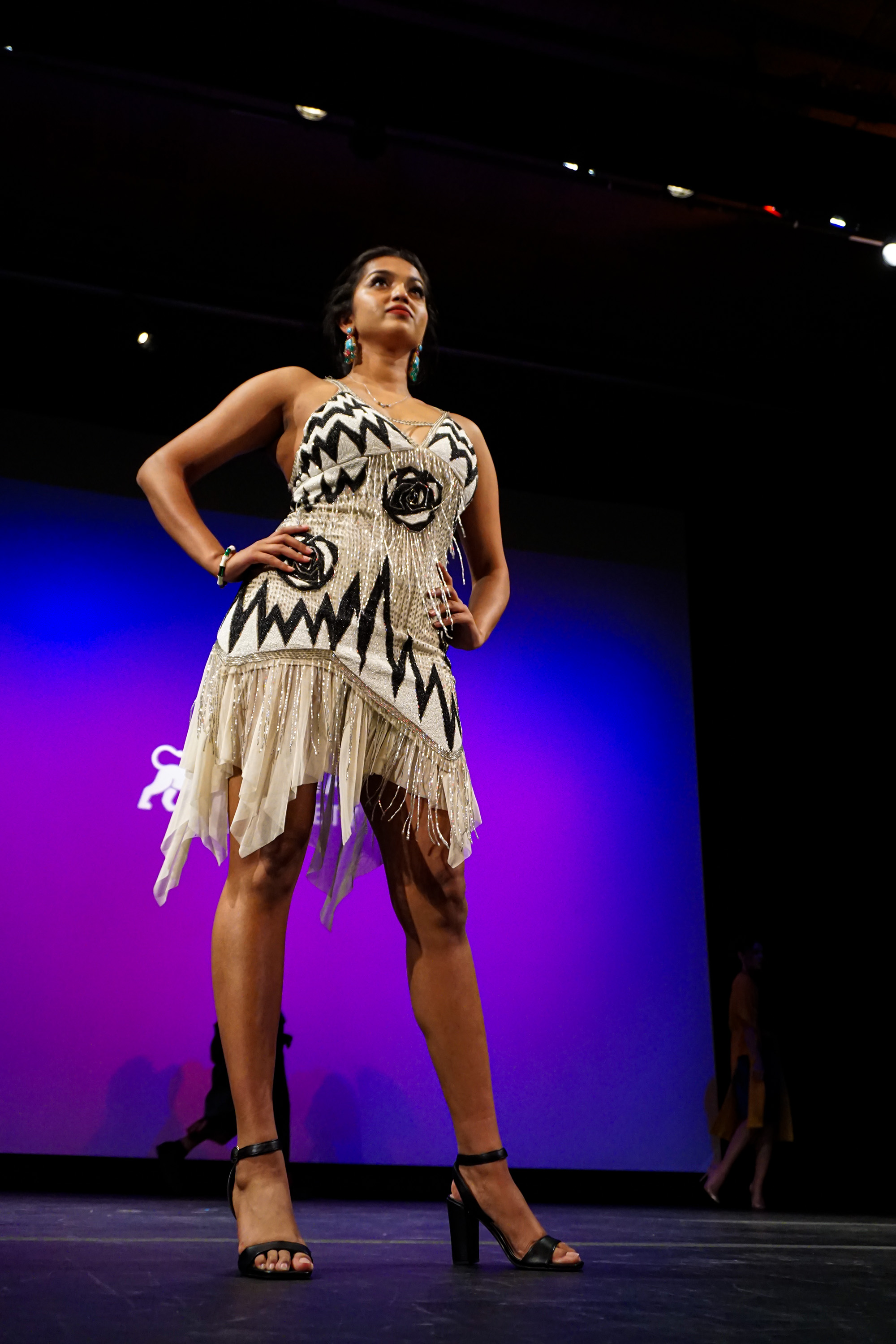 female model posing on stage to a purple background wearing a grey dress