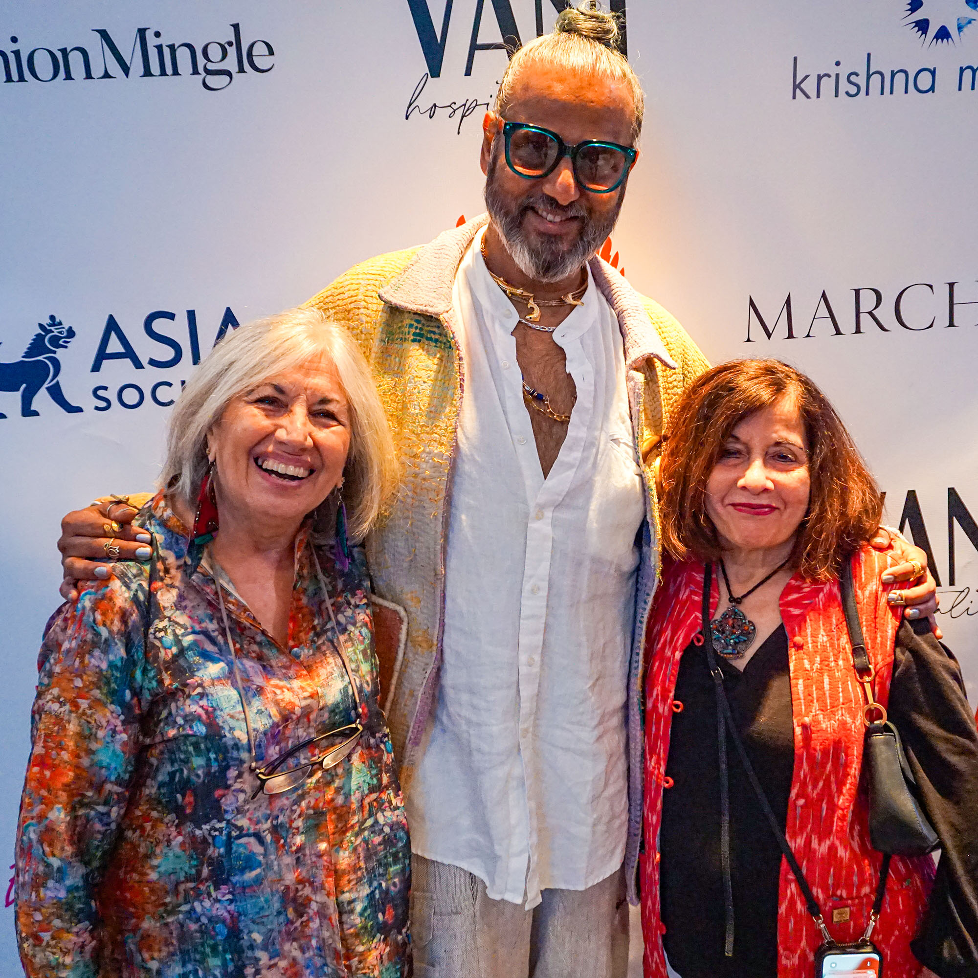 Ajay Shrivastav posing with two women in front of a step and repeat banner