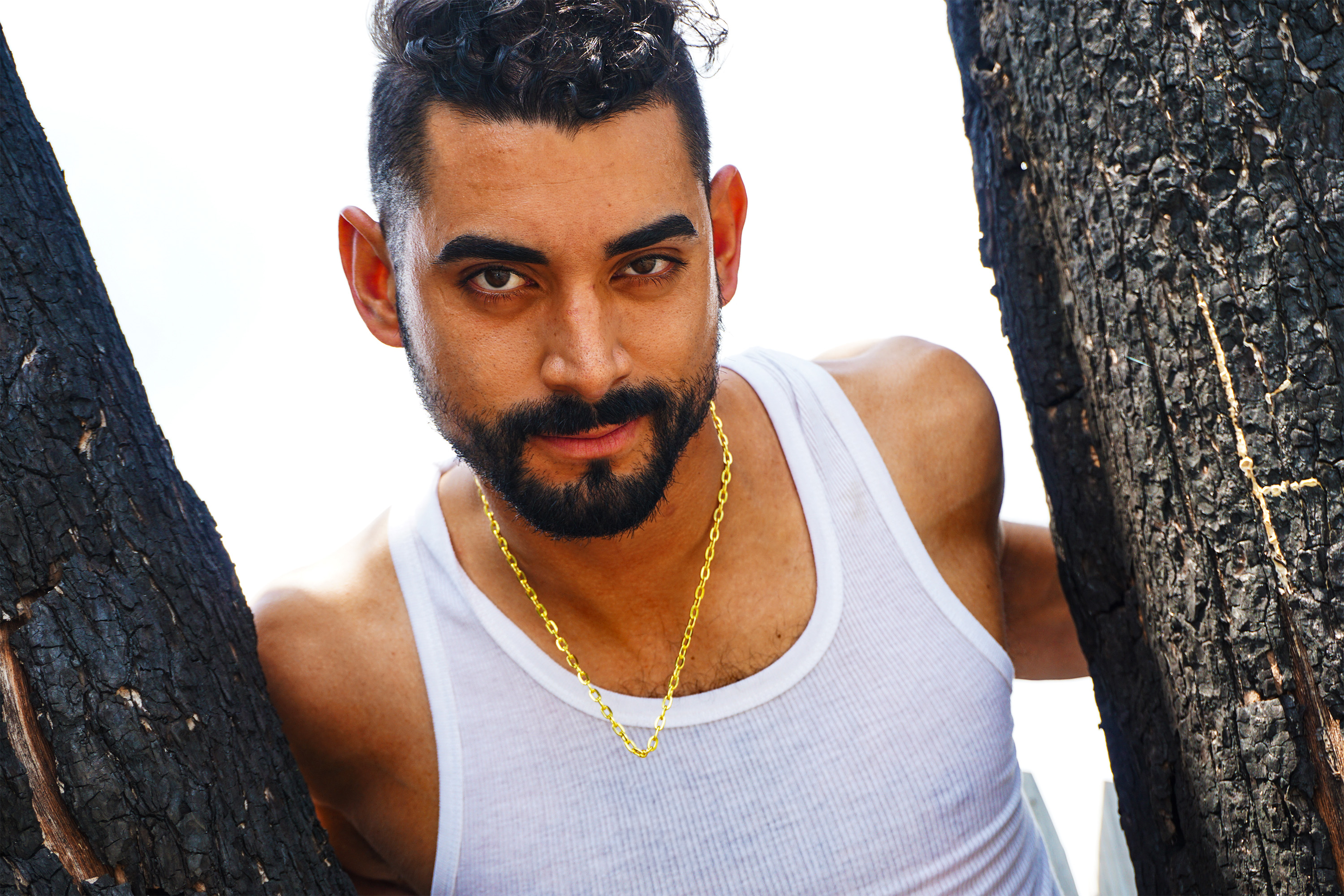 Latin American male model with short and a white beater smirking in between two trees