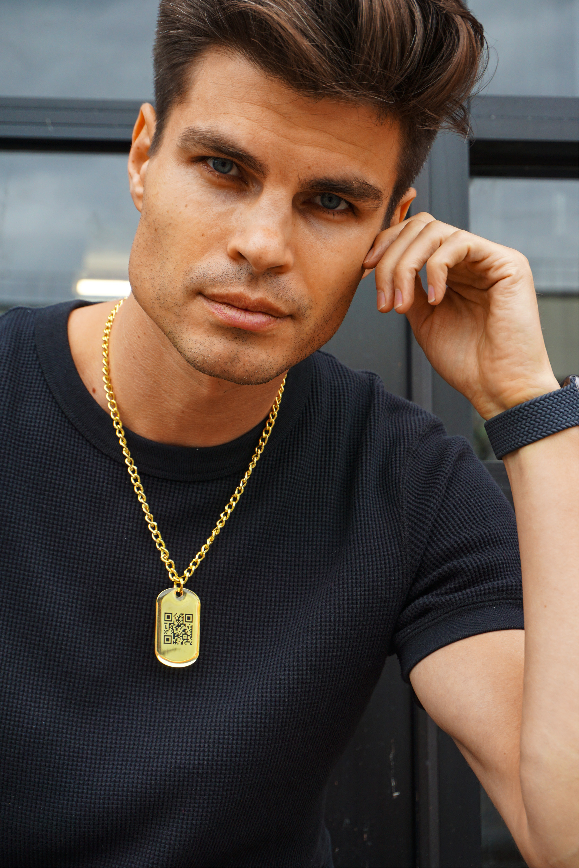 Model Maxim Orlov with his hand to his head wearing a black shirt and a golden QR jumptag dog tag