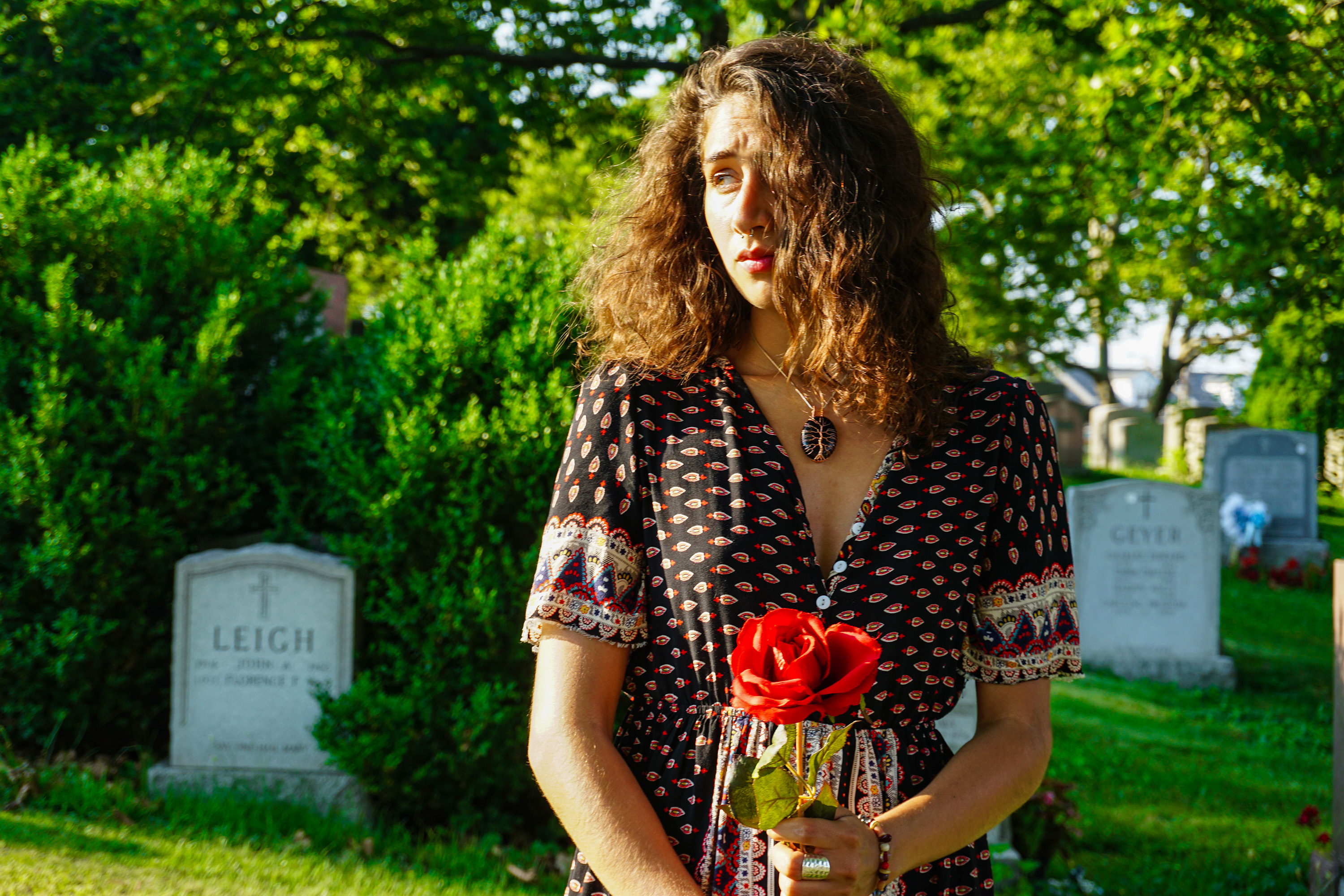 Jibberish Jazzy Jay modeling at a cemetery holding a red rose with hair blowing looking off to the side