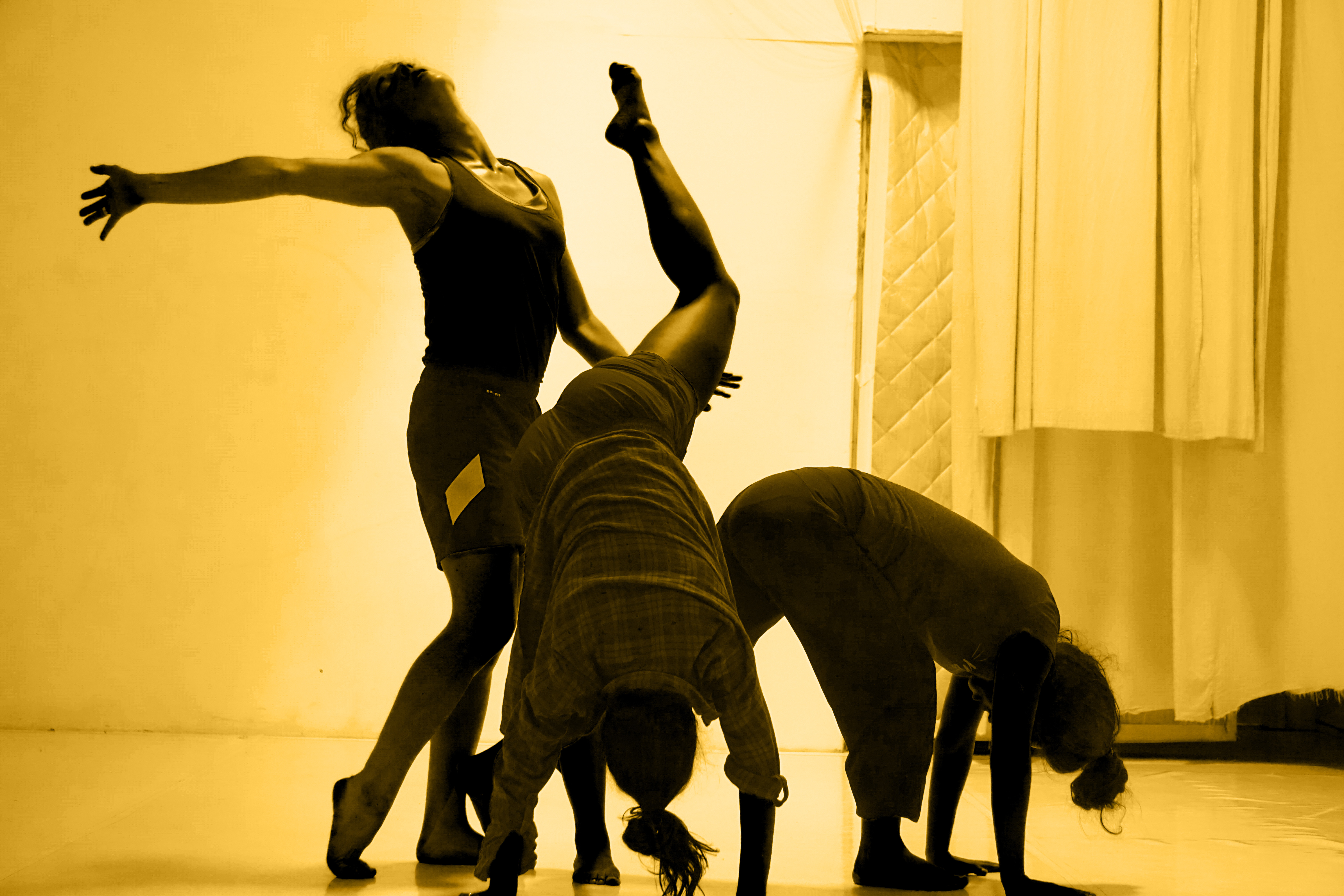 three dancers posing together in a yellow lens aesethetic with two having their hands on the ground and one with her hands up