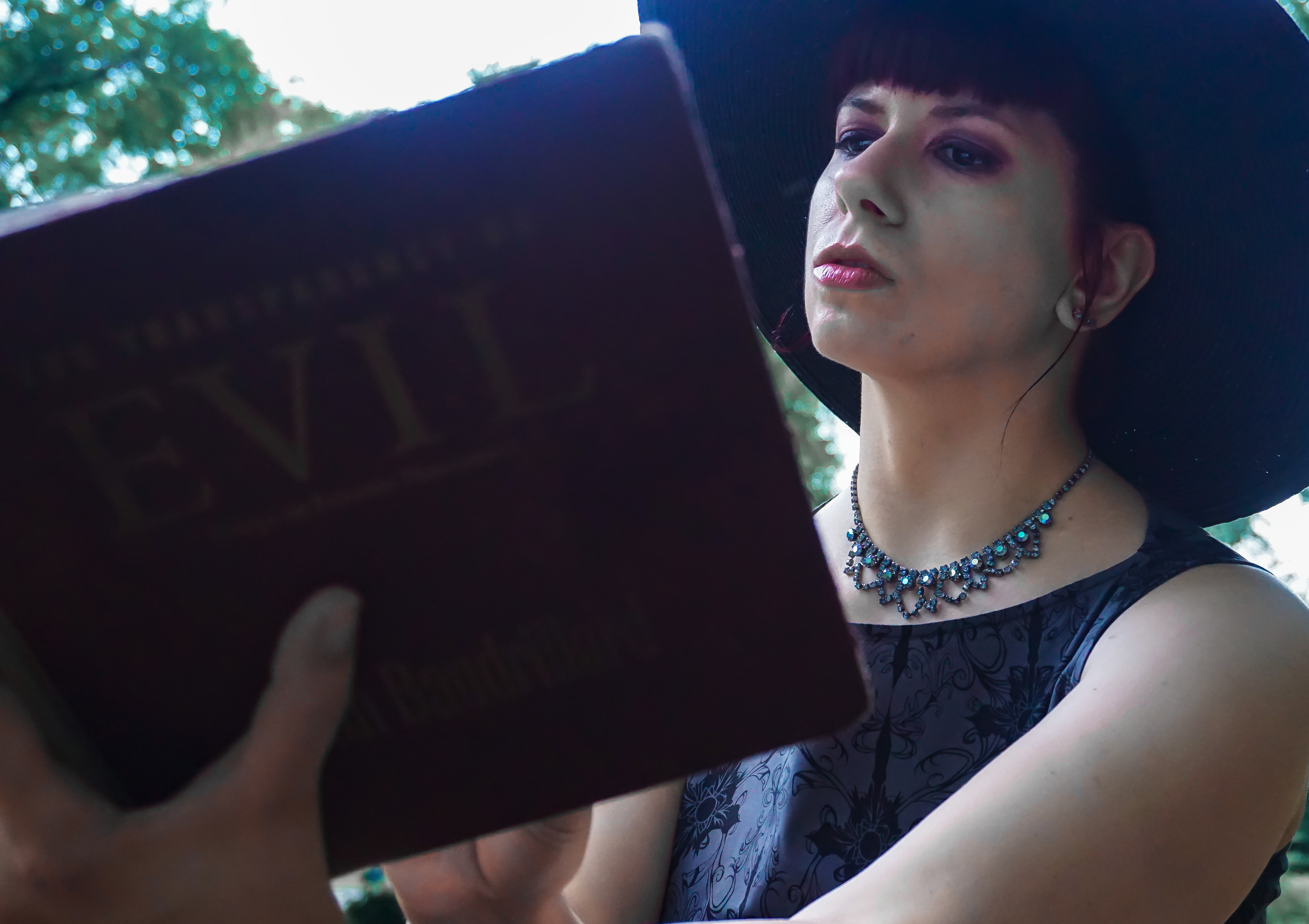 pale woman with big hat reading Jean Baudrillard "Transparency of Evil" book