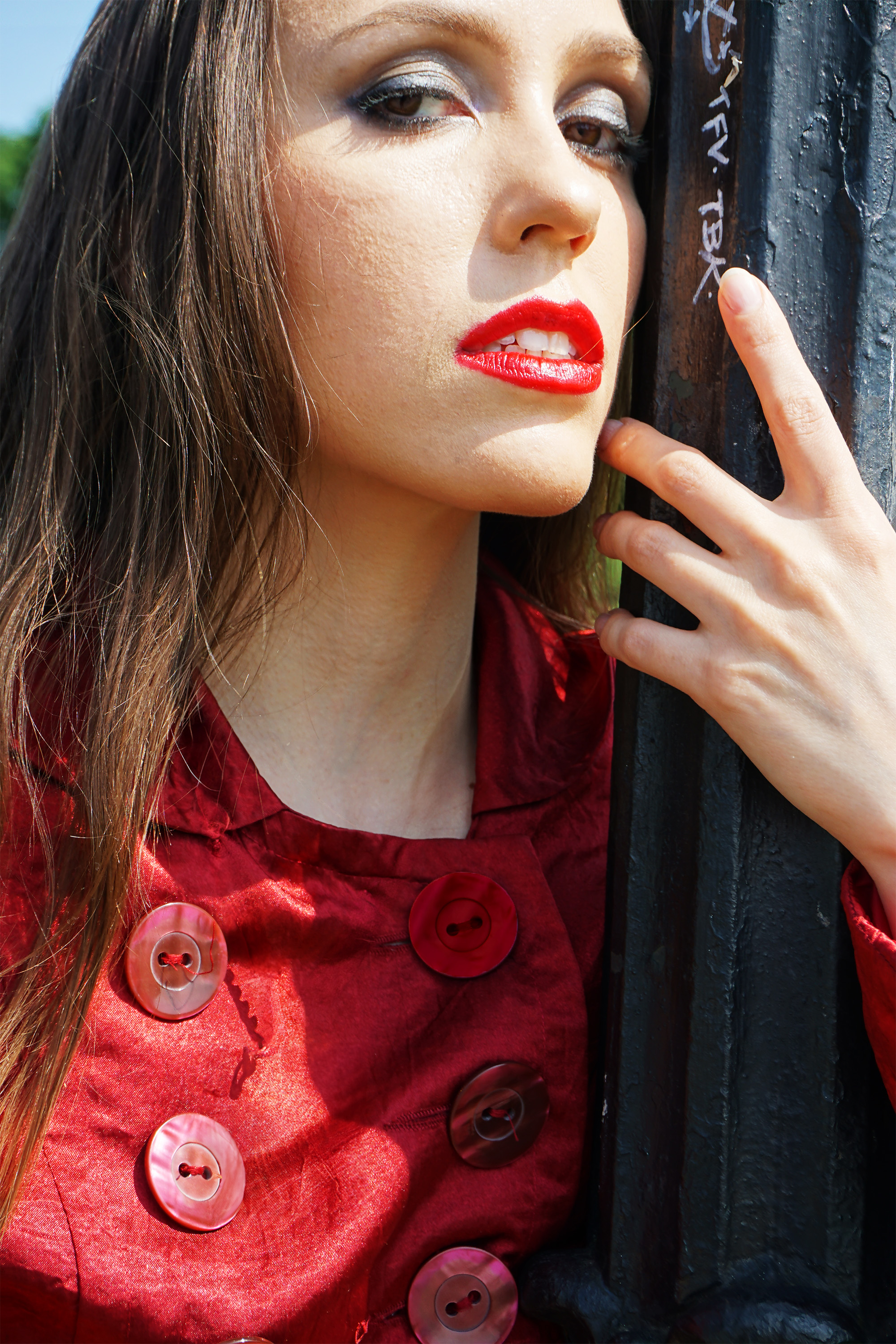 Close up of a female model wearing red lipstick and a red jacket with hand wrapped around light post